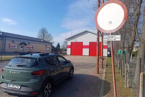 Zielony Dacia Sandero zaparkowany przy remizie OSP. Znak zakazu wjazdu, który nie dotyczy pojazdów OSP, może sugerować mandat za wjazd pod zakaz.