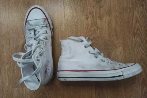 Białe trampki na drewnianym tle. Pokazują, jak wiązać trampki, z luźno zwisającymi sznurówkami.
