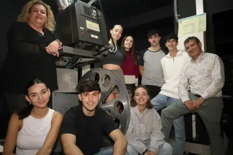 Grupo de jóvenes y adultos posan junto a un proyector antiguo en el cine Cerbuna de Zaragoza.