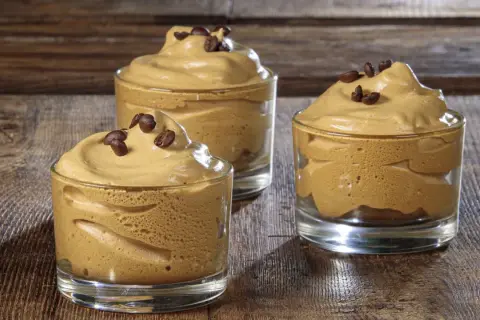 Tre bicchierini di soffice crema di caffè con caffè solubile, guarniti con chicchi di caffè, su un tavolo di legno.