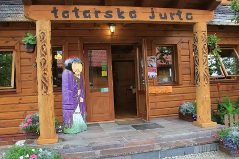 Drewniana fasada z napisem "tatarska jurta". Przed wejściem stoi kolorowa rzeźba postaci w stroju tatarskim.