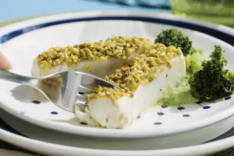 Filetti di merluzzo surgelati, impanati con pistacchi croccanti, serviti con broccoli e una salsa verde.