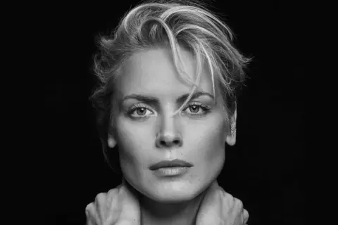 Synnøve Macody Lund, mit ihrem markanten Blick und den Händen am Hals, posiert in einem dramatischen Schwarz-Weiß-Porträt.