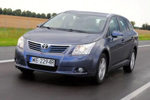 Szary Toyota Avensis T27 1.8 benzyna w kombi jedzie po drodze, za nim pola.