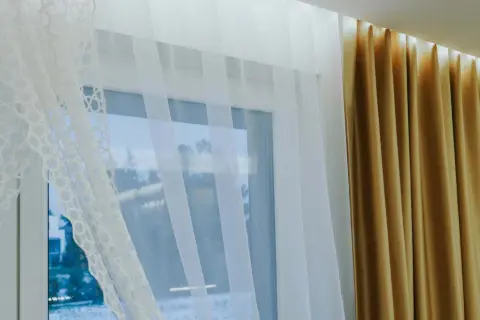 Eleganckie zasłony i firany na jednym karniszu tworzą przytulną atmosferę. Biała, ażurowa firanka i złote zasłony pięknie się komponują.
