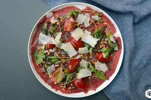 Carpaccio de bœuf finement tranché, garni de tomates cerises, roquette, pignons de pin et copeaux de parmesan. Un délice visuel et gustatif.