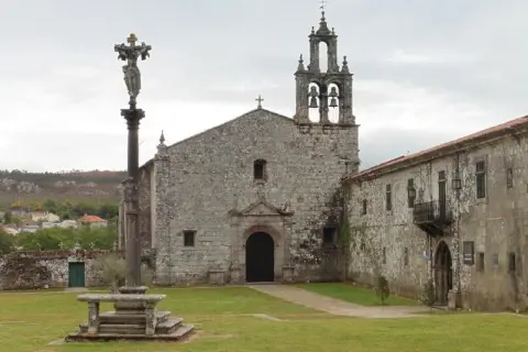 El monasterio de Aciveiro, con su iglesia de piedra y campanario, se alza majestuoso. Un cruceiro antiguo preside el patio.