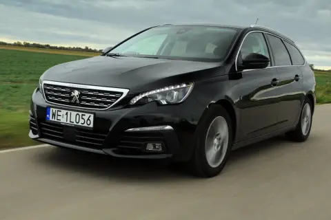 Czarny Peugeot 308 kombi z 2015 roku jedzie po drodze wśród zielonych pól.