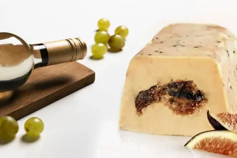 Bouteille de vin blanc à côté d'un bloc de foie gras aux figues, avec des raisins verts et des quartiers de figues. Un délice pour les amateurs d'alcool et de foie gras.