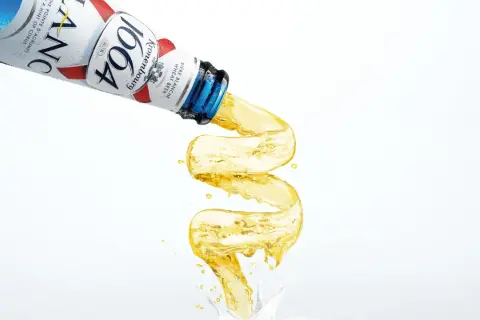 Piwo w niebieskiej butelce Kronenbourg 1664 leje się w fantazyjny sposób, tworząc złoty strumień.