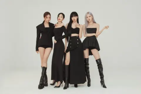 Cztery członkowie BLACKPINK w czarnych, stylowych strojach pozują do zdjęcia.