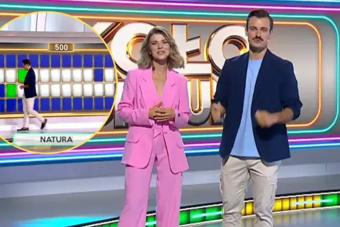 Prowadzący Koło Fortuny na tle planszy z literami i neonowych dekoracji.