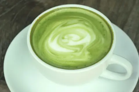 Zielony, spieniony napój w białej filiżance na spodku. To matcha latte, co to za napój?