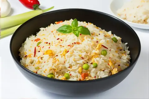 Un bol de riz pilaf aux petits pois, œuf et piment, garni d'une feuille de basilic.