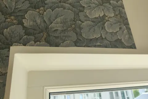Detaljbild av en vägg med blått blommönster, visar hur tapetserar man runt ett fönster.