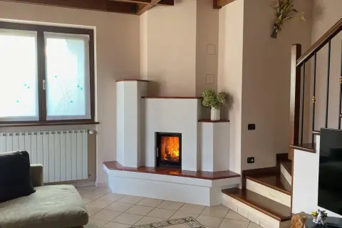 Camino moderno con fiamme vive. La struttura in **calce resiste alle alte temperature**, creando un angolo accogliente con scala e divano.