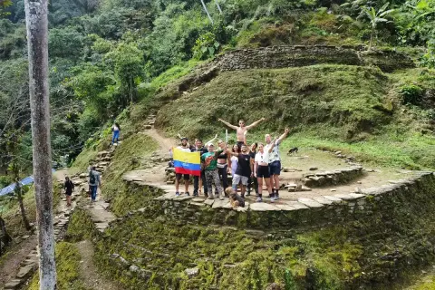 Grupo de turistas celebra en la **ciudad perdida Colombia**, rodeados de ruinas ancestrales y exuberante vegetación.