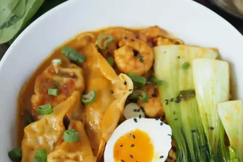 Schüssel mit Ramen, Garnelen, Gyoza, Pak Choi, Ei und Frühlingszwiebeln. Köstliche Ramen-Toppings!