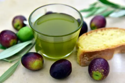 Olio extra vergine d'oliva e olive fresche, eccellenza dei prodotti DOP Puglia, accompagnati da una fetta di pane.