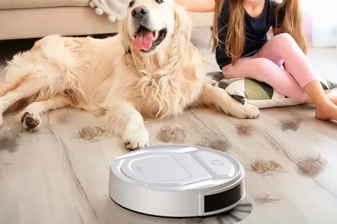 Un robot aspirador limpia el pelo de perro en un hogar mientras una niña acaricia a su mascota.