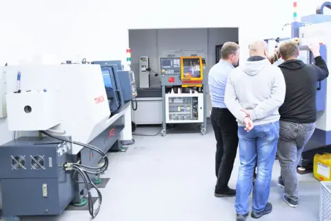 Obrabiarki CNC: co to jest? Grupa mężczyzn ogląda nowoczesne maszyny w hali produkcyjnej.