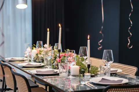 Tavola apparecchiata con candele, fiori rosa e bicchieri per un elegante servizio alla francese.