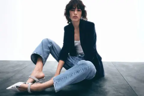 Frau in lässigen Jeans, Samtblazer und glitzernden Mules. Ein Look, der casual chic perfekt verkörpert.