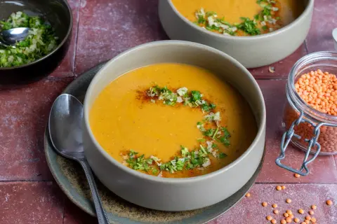 Herzhafte mercimek corbasi, eine cremige Linsensuppe, garniert mit frischen Kräutern und Gewürzen. Daneben eine Schale mit roten Linsen.
