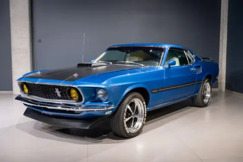 Błękitny Ford Mustang Mach 1 z 1969 roku, z czarną maską i żółtymi światłami, prezentuje się imponująco.