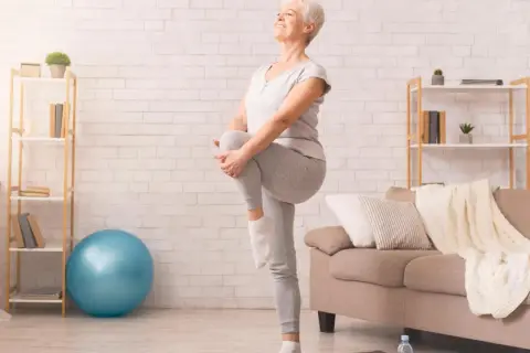 Une femme âgée sourit en faisant un exercice d'équilibre, idéal pour une fiche technique gym douce pour personne âgée.