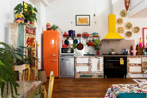 Cuisine colorée avec frigo orange vif, vaisselle suspendue et une astuce rangement cuisine : des portes de placard dépareillées pleines de charme.