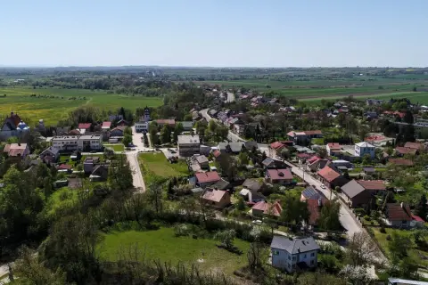 Widok z lotu ptaka na malowniczą wieś, która może pochwalić się mianem najmniejszego miasta w Polsce. Domy z czerwonymi dachami, kościół i zieleń pól tworzą sielski krajobraz.