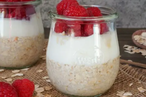 Zwei Gläser mit overnight oats mit joghurt und frischen Himbeeren. Ein gesunder Start in den Tag.