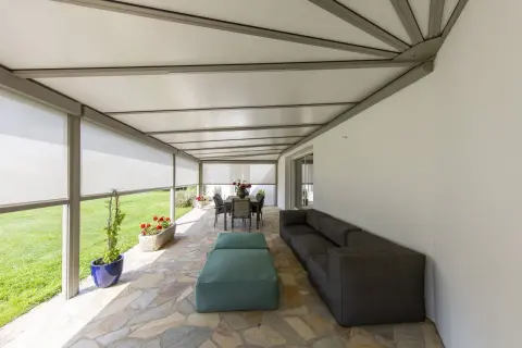 Telo per pergolato fissato con sistema a scomparsa, creando un'area relax con divano e tavolo da pranzo.
