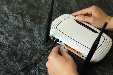 Ręka podłącza kabel sieciowy do routera, rozpoczynając konfigurację sieci domowej.