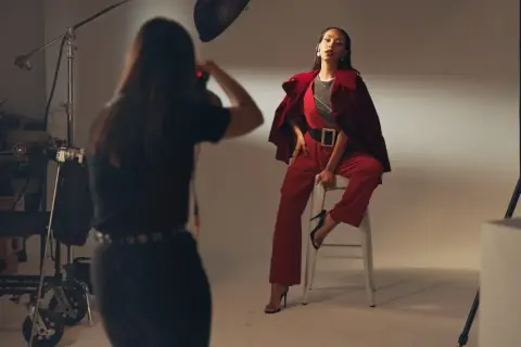 Modelka w czerwonym garniturze pozuje do zdjęcia. Fotografka pracuje, zastanawiając się, ile zarabia fotograf.