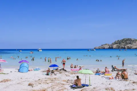 Słoneczna plaża na Majorce, pełna ludzi kąpiących się i opalających. Idealne miejsce na wakacje z dziećmi, oferujące mnóstwo atrakcji.