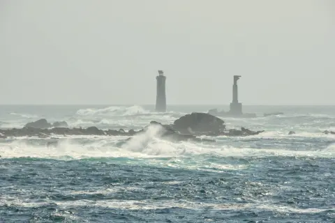 Deux phares se dressent sur des îlots rocheux battus par les vagues, au large de l'île d'Ouessant.