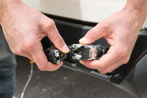 Mains de personne effectuant le branchement prise caravane. Connexion d'un connecteur électrique à une prise sur un véhicule.
