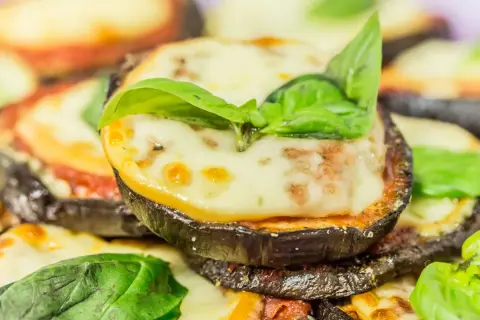 Fette di melanzane cotte al forno, ricoperte di sugo di pomodoro, mozzarella filante e basilico fresco. Un piatto invitante di melanzane alla pizzaiola.
