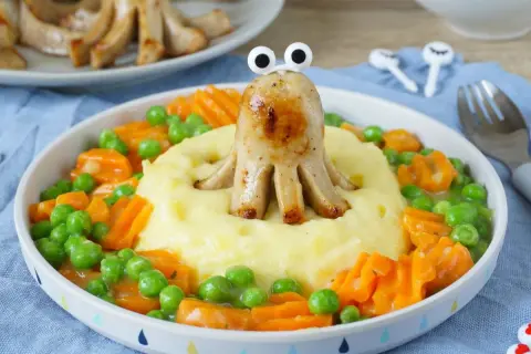 Ein lustiger Tintenfisch aus Bratwurst vom Vortag, der aus Kartoffelbrei mit Erbsen und Karotten schaut.