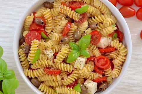 Un piatto invitante di pasta fredda con pomodorini, olive, cubetti di mozzarella e basilico fresco. Perfetta per un'estate gustosa.