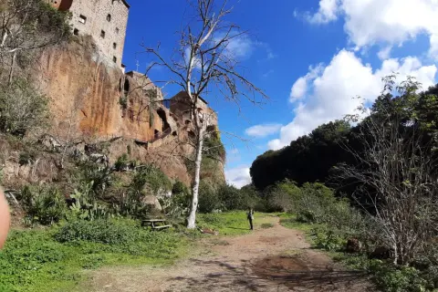 Sentiero verso Castel Sant'Elia, cosa vedere: roccia imponente, vegetazione rigogliosa e un cielo azzurro con nuvole bianche.