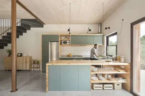 Hombre lavando platos en una cocina moderna y luminosa, ideal para renovar cocina con estilo minimalista y materiales naturales.
