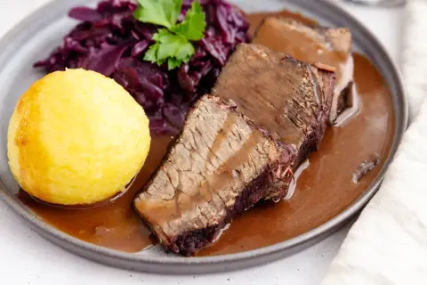 Original Sauerbraten: zartes Rindfleisch in dunkler Sauce, serviert mit Rotkohl und Klößen.