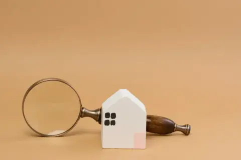 Lente d'ingrandimento su una casetta bianca, per capire cos'è una visura catastale e i dettagli di un immobile.