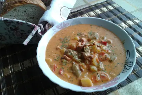 Pyszny, sycący bogracz z ziemniakami i mięsem, posypany natką pietruszki, obok koszyk z chlebem.