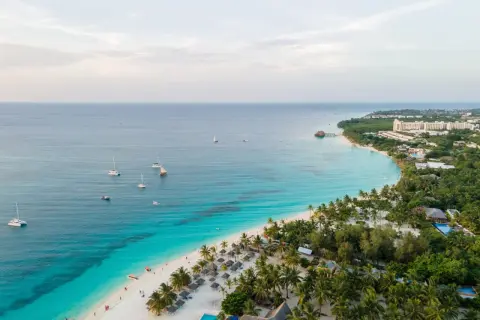 Rajska plaża na Zanzibarze z turkusową wodą, palmami i łodziami. Sprawdź aktualne zanzibar ceny, by zaplanować wymarzone wakacje.