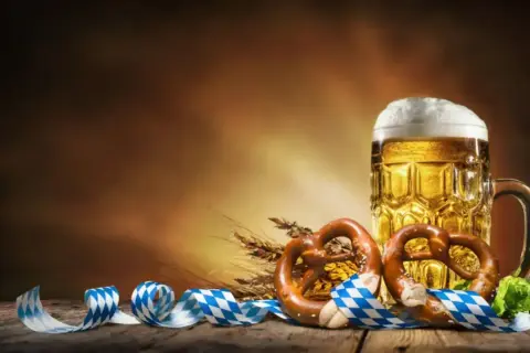 Boccale di birra dorata, pretzel e nastri bavaresi evocano la storia dell'Oktoberfest.