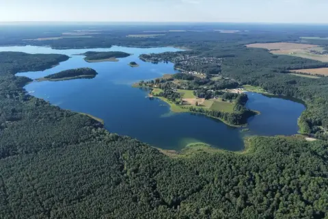 Malownicze jezioro Niesłysz otoczone lasami, z widocznymi wysepkami i zabudowaniami na brzegu.